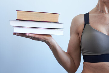 Woman in sports bra holding a stack of books on grey background. The concept is power in knowledge.