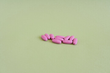 Pink pills on a green background. Focus on foreground, soft bokeh.