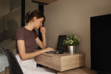 A girl works on a laptop at a table at home.