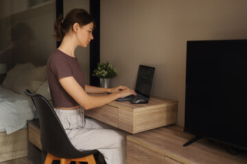 A girl works on a laptop at a table at home.
