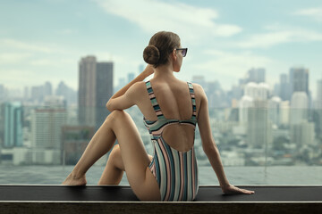 A woman sunbathes by a rooftop pool overlooking the city's skyscrapers.