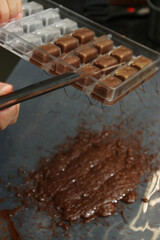 chef's hand flipping chocolate mould to empy cavities for praline