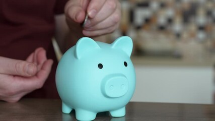 Closeup of hand repeatedly dropping coins into pastel blue piggy bank, representing systematic saving and strategic financial planning for long-term wealth accumulation