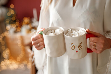 A woman in white clothes holds two white mugs in her hands