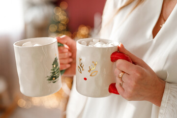 A woman in white clothes holds two white mugs in her hands