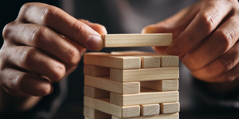 Close-up of hands placing wooden block on tower, showcasing strategy, risk, and planning concepts.  Represents careful decision-making and balance.