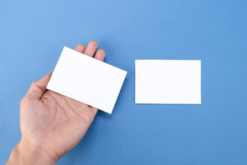Fototapeta premium Hand holding white blank business card mockup on blue background
