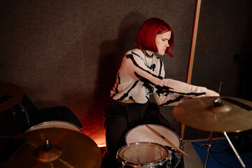 Side view of young female musician focusing on adjusting cymbals preparing drum set before...