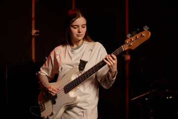 Medium full shot of young female artist playing electric bass guitar enjoying giving performance on...