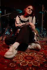 Full shot of teenage female drummer wearing spiked choker necklace looking confidently at camera,...