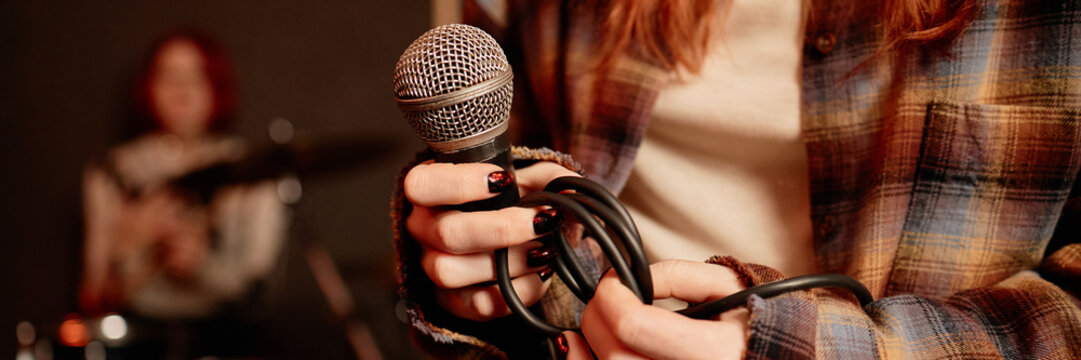 Website header shot of wire microphone in hands of female vocalist performing music with band in recording studio - Powered by Adobe