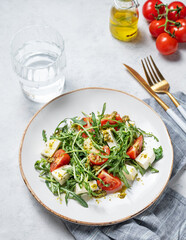Healthy arugula salad with cherry tomatoes, mozzarella and pesto sauce on a plate