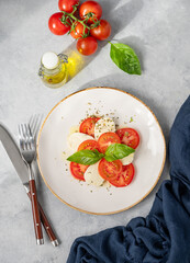 Caprese salad with sliced ​​tomatoes, mozzarella and basil on a plate on a light background