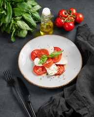 Caprese salad with sliced ​​tomatoes, mozzarella and basil on a plate on a dark background