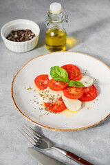 Caprese salad with sliced ​​tomatoes, mozzarella and basil on a plate on a light background