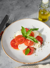 Caprese salad with sliced ​​tomatoes, mozzarella and basil on a plate on a blue background