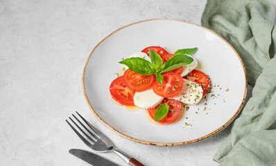 Caprese salad with sliced ​​tomatoes, mozzarella and basil on a plate on a light background