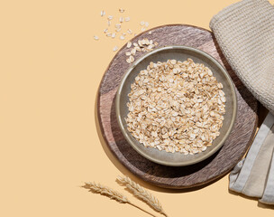 Oat flakes in bowl with wheat and napkin on a wooden board on a yellow background.
