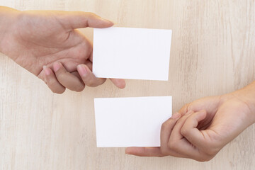 Obraz premium Hand holding white blank business card mockup on wooden background