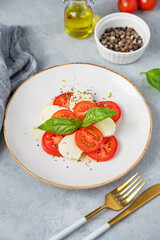 Caprese salad with sliced ​​tomatoes, mozzarella and basil on a plate on a light background