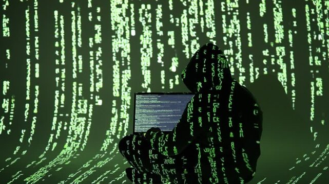 A cybercriminal in a hooded outfit types on a laptop surrounded by digital green code. This immersive matrix-style scene reflects cybercrime, hacking, and data breaches in progress