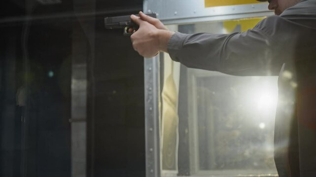 Backlit tilting closeup of face and hands of man in baseball cap, earmuffs loading magazine into semi-automatic gun, racking, aiming firearm at target and shooting while practicing skills at gallery