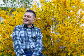 portrait of a man on the background of yellow forsythia flowers, spring nature and blossoms