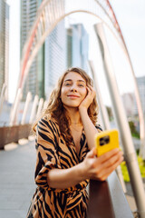 Cheerful woman in stylish clothes with a phone against the backdrop of a metropolis. A young...