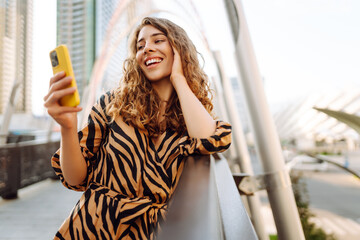 Cheerful woman in stylish clothes with a phone against the backdrop of a metropolis. A young...