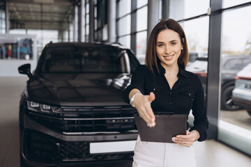 Saleswoman offering handshake in front of new car in a dealership