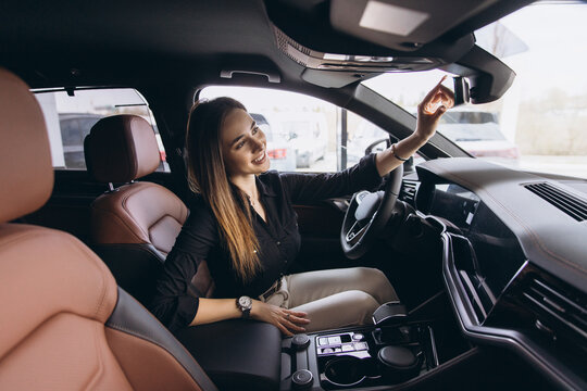Elegant businesswoman adjusting rearview mirror, sitting in new car at dealership