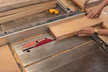 Close-up of hands guiding a wooden board through a table saw with a red blade, used for precise...