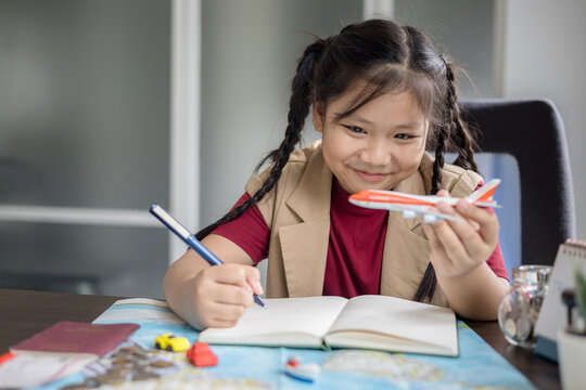 Girl is holding a model airplane and smiling happily while planning her travel on the table