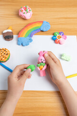child's hands playing with colorful plasticine on wooden table.