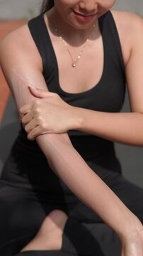 Young Asian woman applying moisturizing sunscreen lotion on face and body before exercising outdoor.