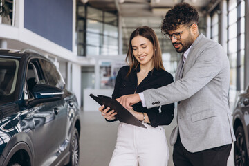 Car salesman showing contract to customer buying new car in dealership