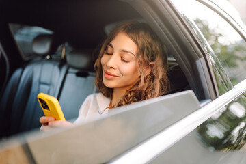 Portrait of a young business woman with a phone sitting on the backseat of a car. Beautiful woman...