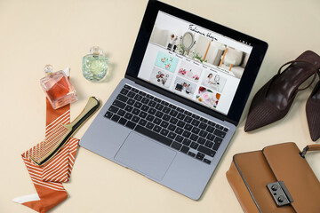 Laptop with fashion blog web site, shoes, accessories and perfumes on beige background, above view