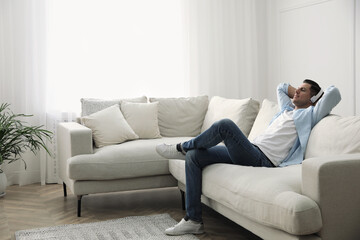 Fototapeta premium Man with headphones sitting on comfortable sofa in living room