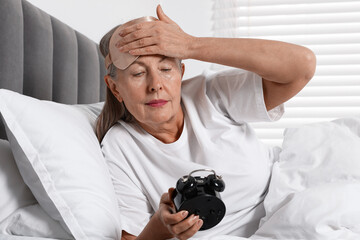 Overslept woman with alarm clock in bed at home
