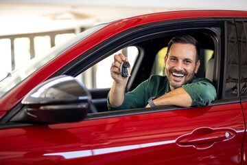 Handsome man raising hand up with the car key and smiling at camera, showing key from his brand new...