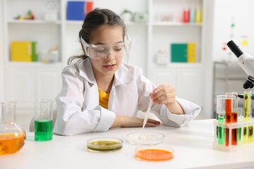 Little girl doing chemical experiment at desk indoors