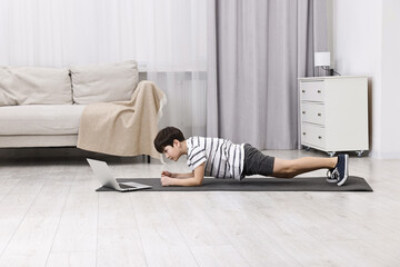 Little boy doing plank exercise near laptop at home. Morning routine