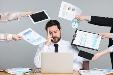 Man overwhelmed by different requests from colleagues at desk on light grey background