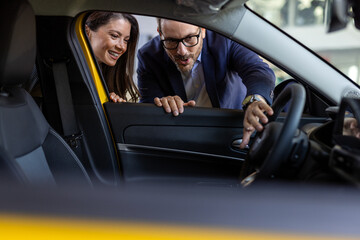 Cute couple sitting in a car at a dealer while deciding whether to buy. Spouses Looking At Car Interior Buying Vehicle In Store. We should organize a test drive