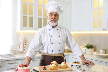 Elderly pastry chef at table with desserts in kitchen