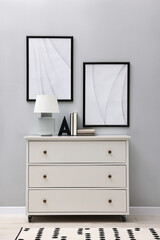 Dresser with table lamp and bookend near light grey wall in room. Interior design