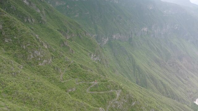 Drone shot from a distance, capturing the trekking path from Cabanaconde to Sangalle, with a resting point visible along the route, surrounded by the dramatic landscapes of Colca Canyon.