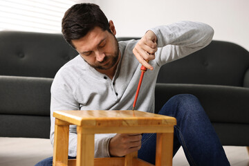 Man repairing wooden stool with screwdriver at home