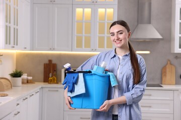 Smiling woman holding bucket with cleaning supplies in kitchen